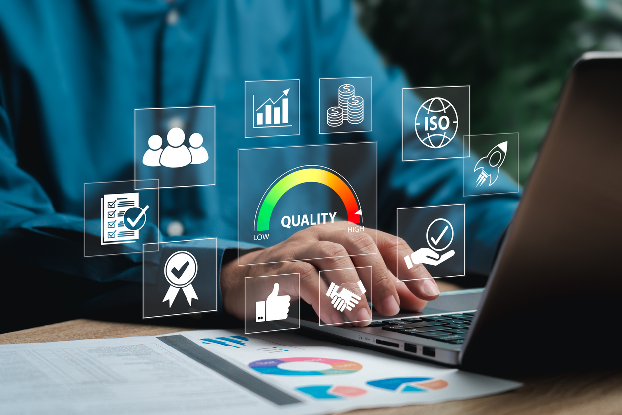 Business professional typing on a laptop with digital icons representing quality assurance, ISO certification, financial growth, teamwork, and performance metrics 